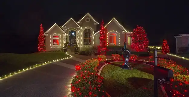 Large single-family home with wraparound driveway at night, lit with red and white holiday lights.